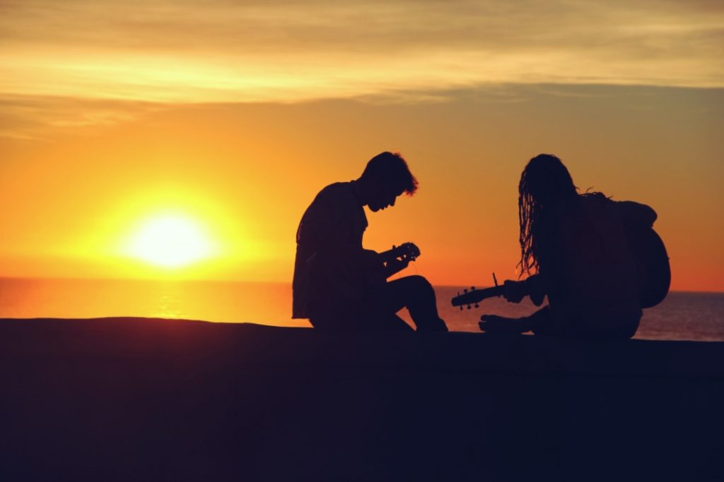 Silueta de dos personas tocando instrumentos en la playa.